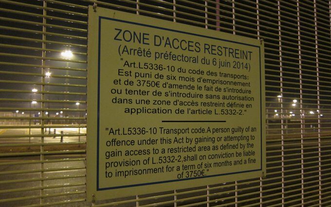 photo du panneau accroché au grillage entourant le terminal de traversée de la Manche à Calais "Zone d'accès restreint, arrêté préfectoral et article en détail)