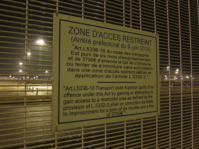 photo du panneau accroché au grillage entourant le terminal de traversée de la Manche à Calais "Zone d'accès restreint, arrêté préfectoral et article en détail)